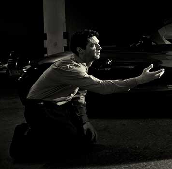 A photograph of a man kneeling in a parking garage, pleading for his life